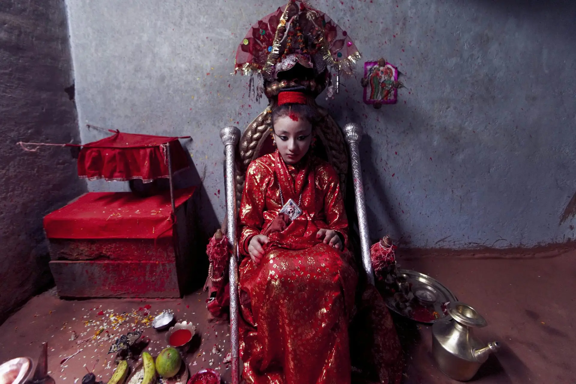 A young girl dressed in traditional attire participates in a cultural religious ceremony indoors.