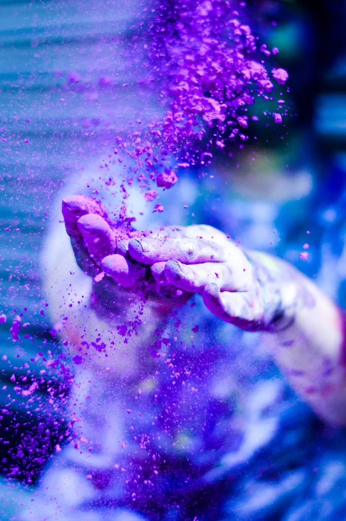 Close-up of hands tossing vibrant purple powder during Holi festival celebration.