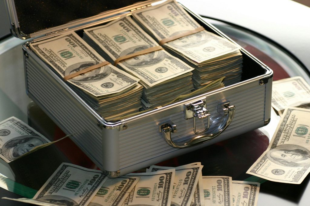 Billionaire cash. Open briefcase filled with stacks of hundred dollar bills on a glass table, representing wealth.